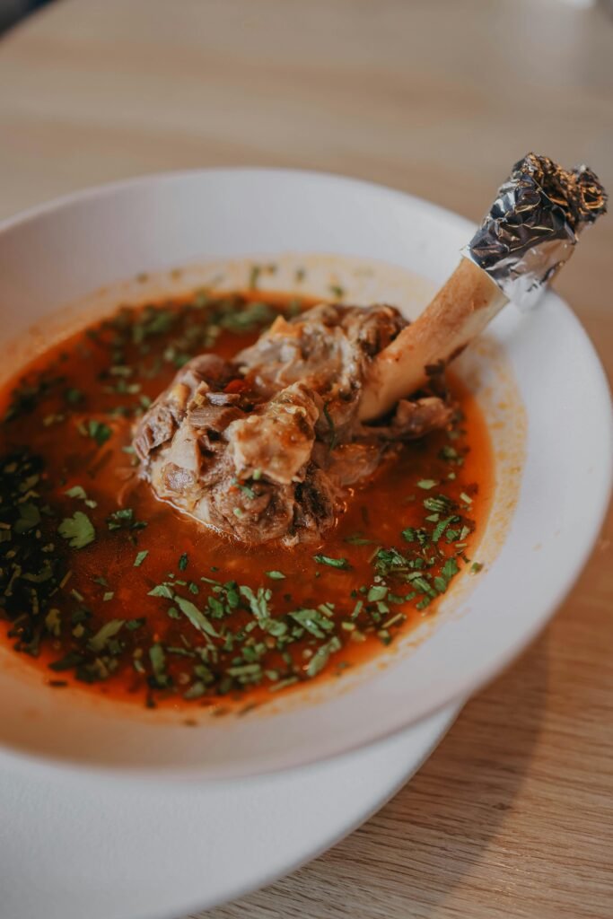 A flavorful lamb shank stew garnished with herbs, served in a white bowl.
