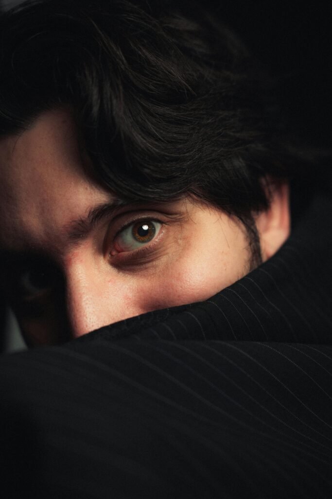 Close-up portrait of a man with intriguing gaze hidden behind a dark coat, creating a mysterious mood.